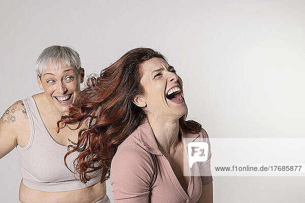 Lachende rothaarige Frau  die Spaß mit ihrer Freundin vor weißem Hintergrund hat