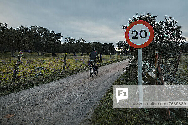 Cyclist riding by speed limit sign on road at sunrise
