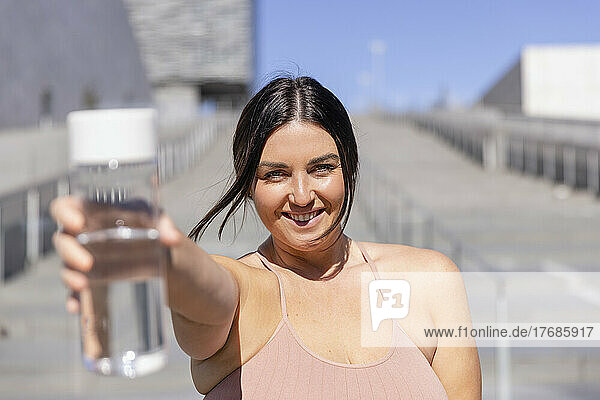 Lächelnde Frau zeigt Wasserflasche vor der Treppe