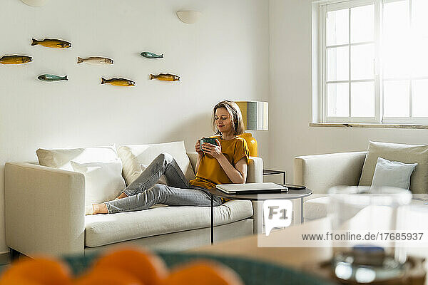 Woman with coffee mug sitting on sofa in living room