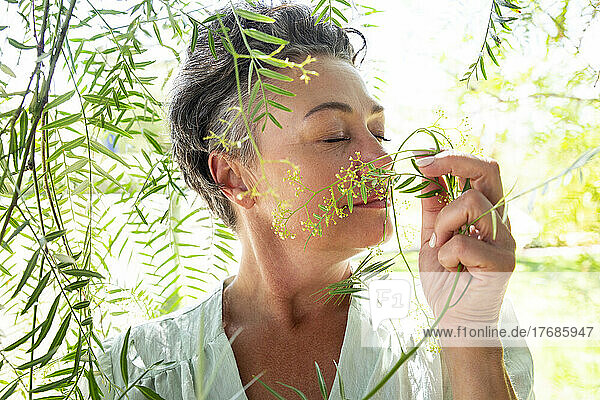 Woman with eyes closed smelling leaves standing in garden