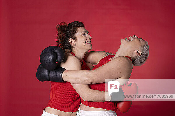Happy friends wearing boxing gloves hugging each other against red background