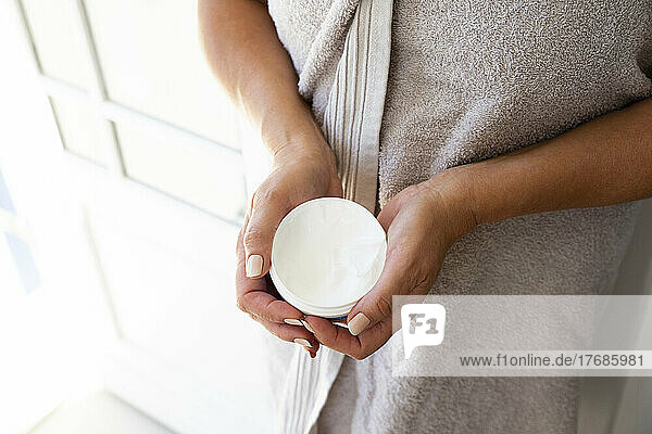 Hands of woman holding container of moisturizer cream