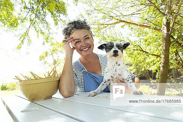 Smiling woman with pet dog at table in garden