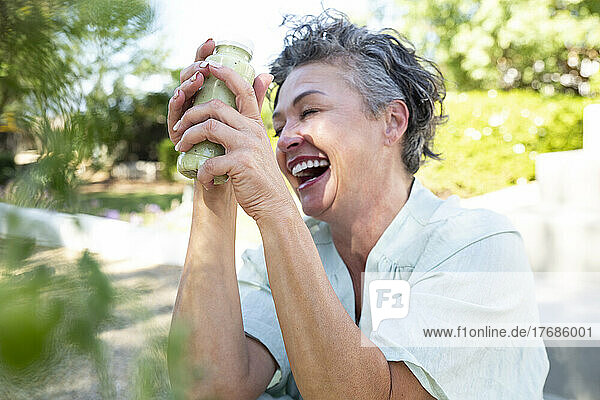 Cheerful woman with bottle of smoothie sitting in garden
