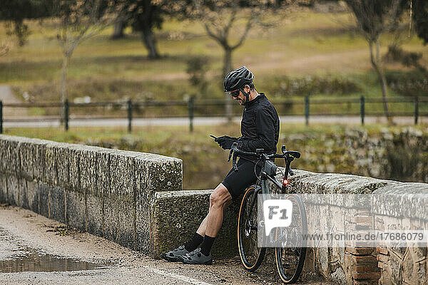 Cyclist using mobile phone leaning on wall