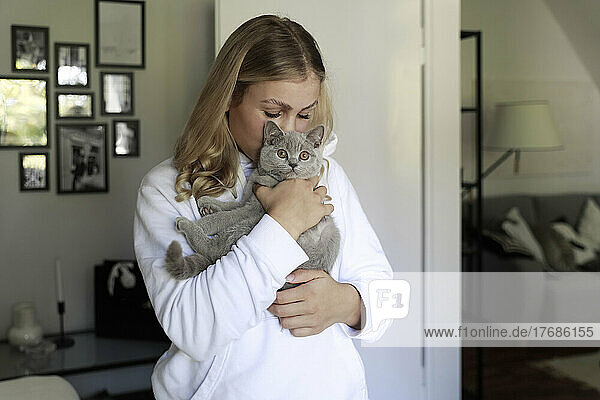 Young woman kissing gray cat at home