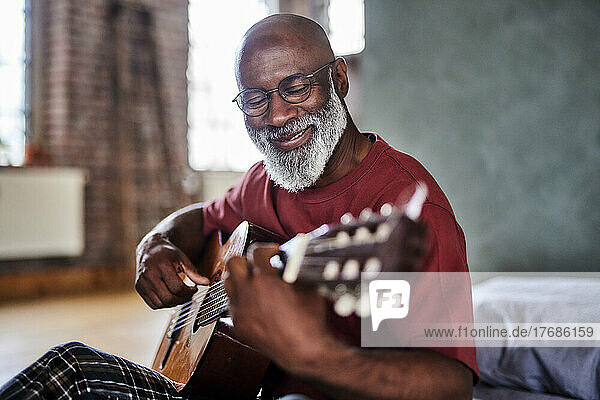 Lächelnder reifer Mann  der zu Hause Gitarre spielt