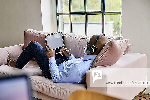 Businessman with headset using tablet PC on sofa at home
