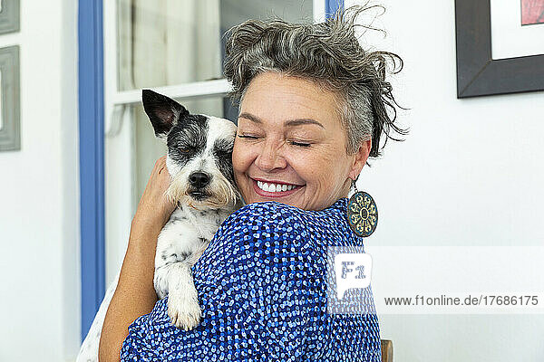 Happy mature woman with short hair embracing dog at home