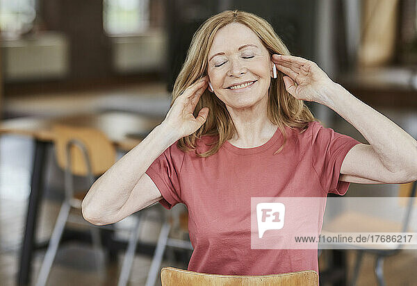 Smiling woman wearing wireless in-ear headphones enjoying music at home