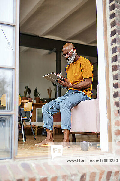 Glatzköpfiger Mann benutzt Tablet-PC und sitzt zu Hause auf dem Sofa