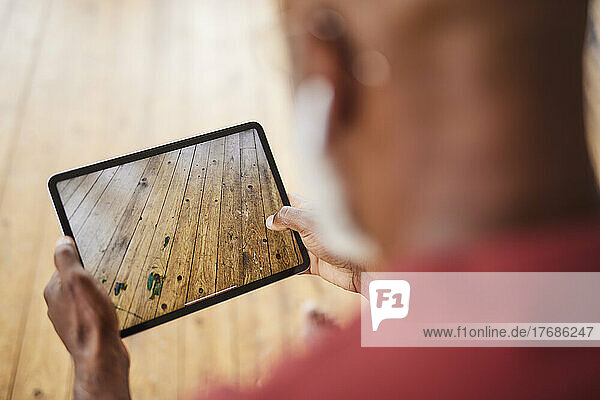 Man photographing hardwood floor through tablet PC at home