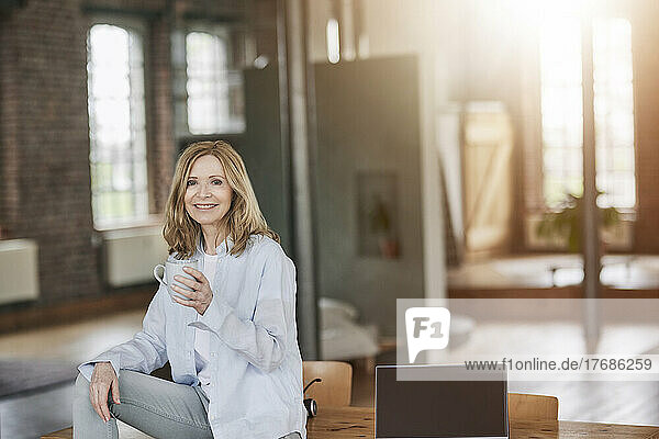 Smiling woman with coffee cup sitting on table at home