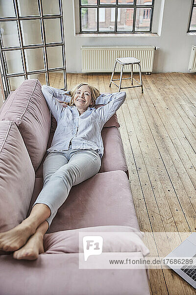 Happy woman with hands behind head lying on sofa at home