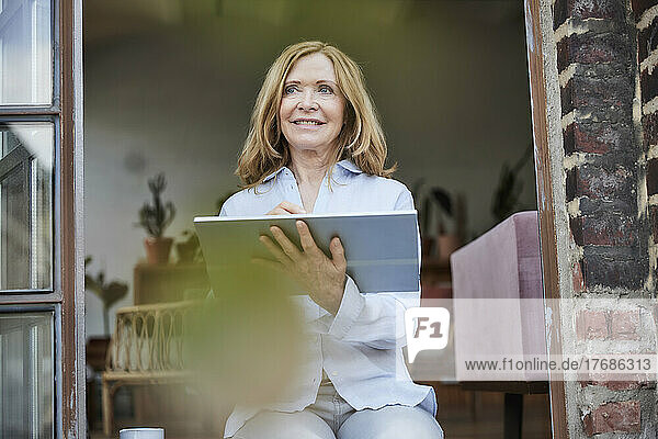 Smiling businesswoman with tablet PC sitting on doorway