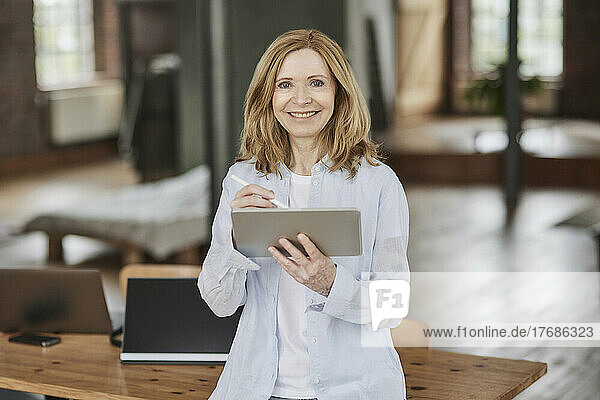 Smiling businesswoman with tablet PC leaning on table at home