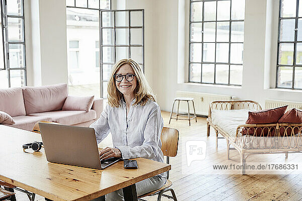 Happy freelancer with laptop sitting at table in living room