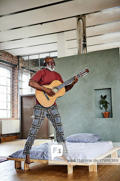 Mature man jumping and playing guitar in bedroom