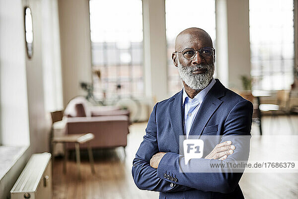 Thoughtful businessman standing with arms crossed at home