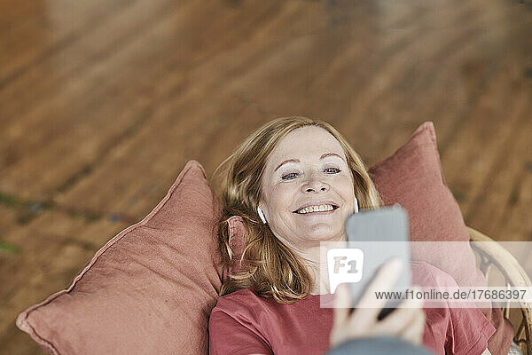 Happy woman using smart phone lying on sofa at home