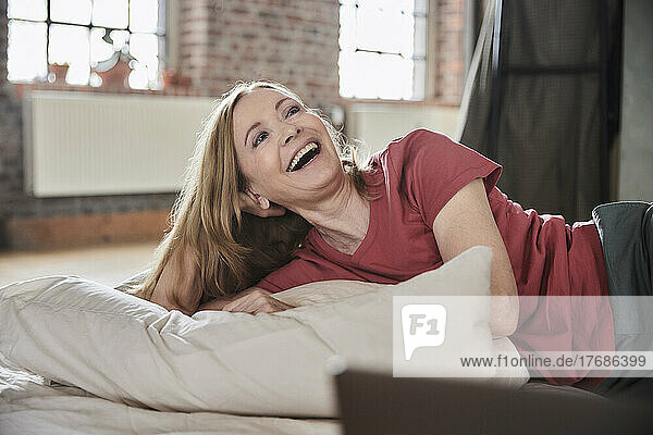 Happy woman with pillow lying on bed at home