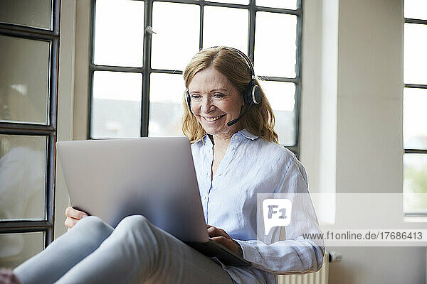 Happy freelancer wearing headset working on laptop at home