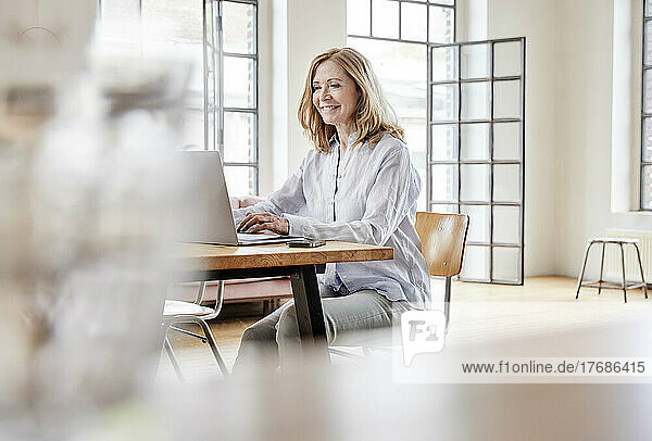 Lächelnder Freiberufler mit Laptop am Tisch im Heimbüro