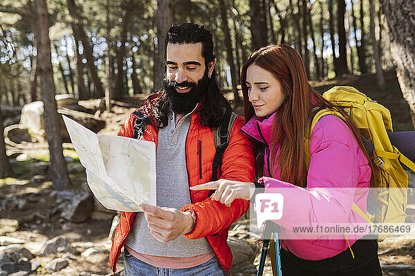 Redhead woman pointing at map held by man standing in forest