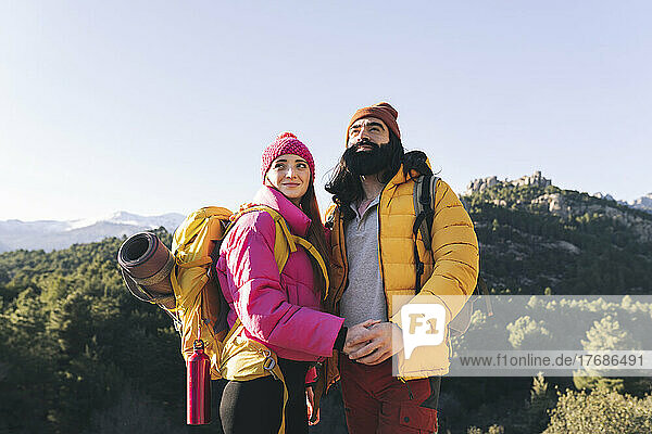Woman wearing backpack standing with bearded boyfriend on sunny day