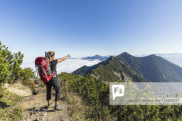 Germany  Bavaria  Female hiker standing at summit of Heimgarten pointing back at Herzogstand