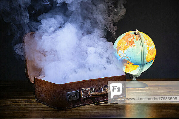 Studio shot of glowing globe and smoke rising from open suitcase