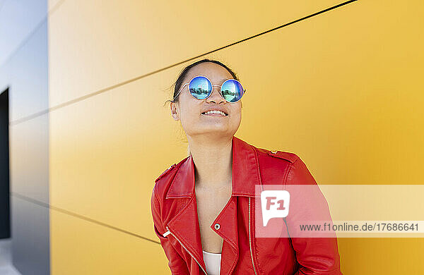 Smiling woman wearing sunglasses standing in front of yellow wall