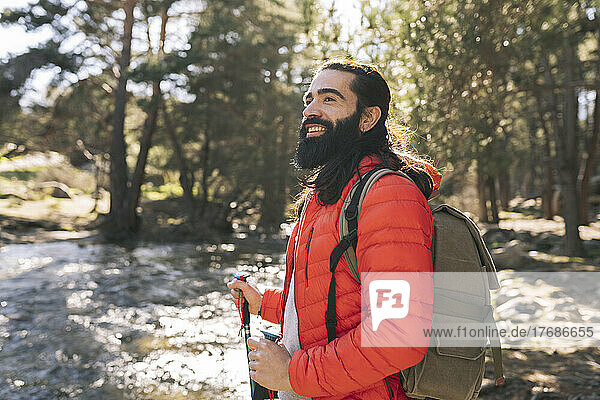 Glücklicher bärtiger Mann mit Rucksack steht im Wald