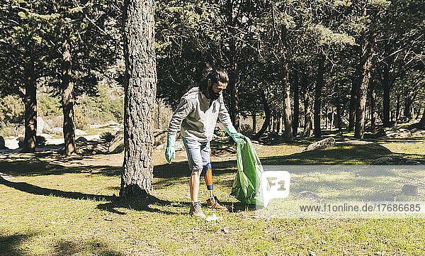 Behinderter Mann mit Müllsack im Wald an sonnigem Tag