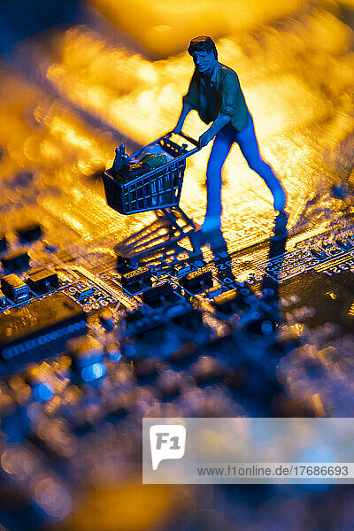 Computer mother board and figurine of man pushing shopping cart symbolizing online shopping