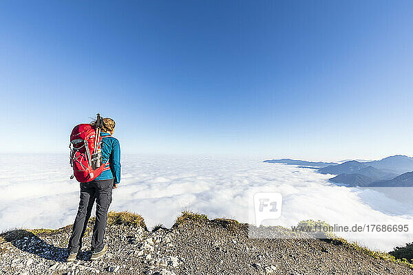 Deutschland  Bayern  Wanderin steht auf einem Berggipfel und bewundert die nebelverhangenen Gipfel der Bayerischen Voralpen
