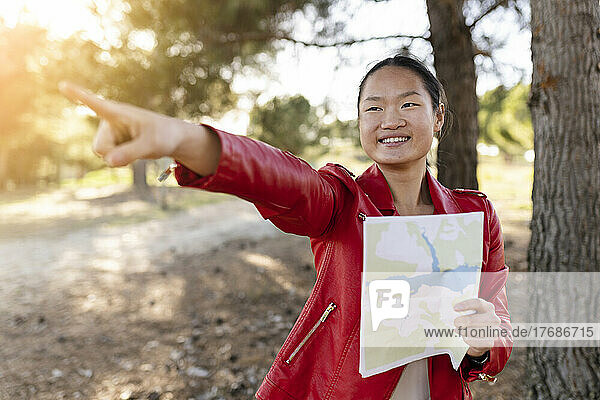 Lächelnde Frau hält Karte in der Hand und gestikuliert im Wald