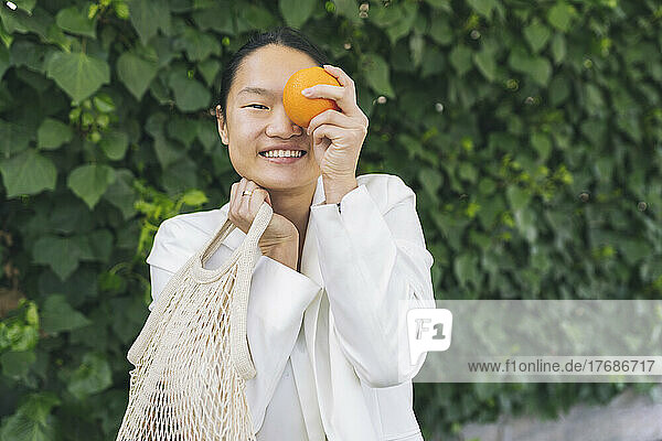 Smiling woman holding orange in front of eye
