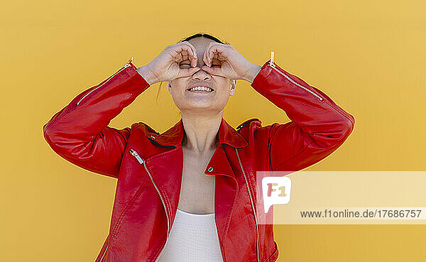 Smiling woman gesturing with hand binoculars against yellow background