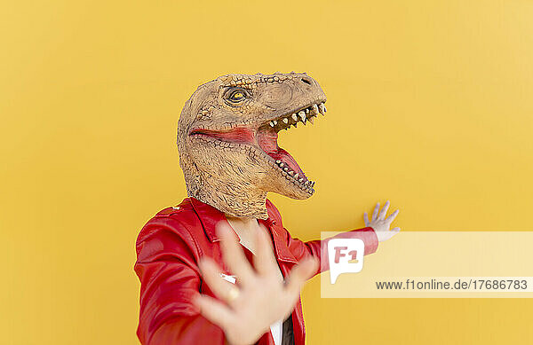 Playful woman wearing dinosaur mask against yellow background