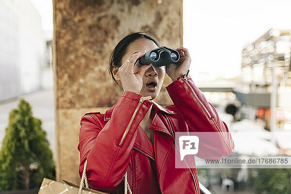 Shocked young woman with mouth open looking through binoculars