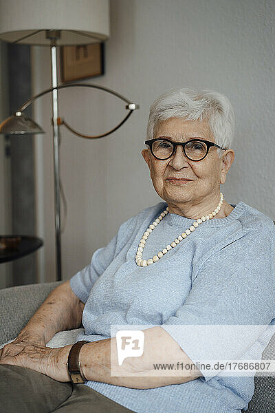 Lächelnde ältere Frau mit Brille sitzt zu Hause auf dem Sofa