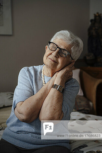 Senior woman with eyes closed leaning head on hands at home