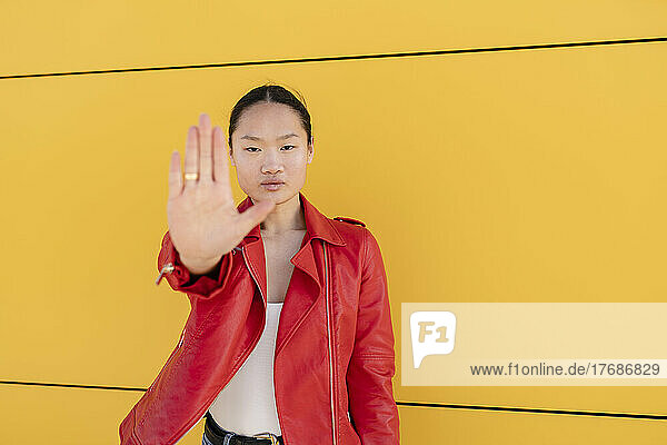 Young woman gesturing stop sign with hand in front of yellow wall