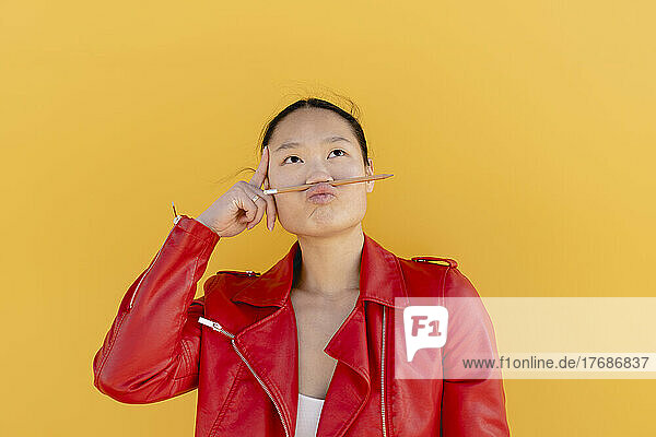 Playful woman with pencil on puckering lips against yellow background