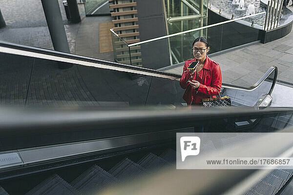 Junge Frau spricht auf der Rolltreppe über den Lautsprecher ihres Mobiltelefons