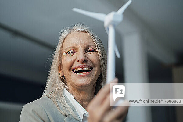 Happy businesswoman holding wind turbine model at office