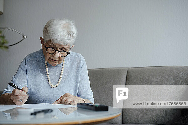 Ältere Frau erledigt Papierkram und sitzt zu Hause auf dem Sofa