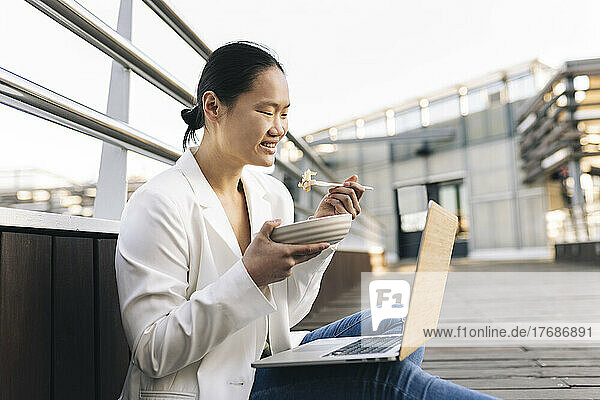 Happy businesswoman eating salad sitting with laptop